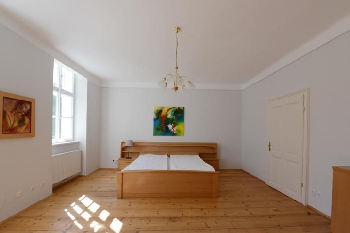 Bedroom with wooden floor, double bed, two paintings and a window.