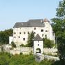 Historic castle with a white façade and battlements, surrounded by trees.