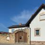 A white house with brown window frames and a stone wall with a wooden gate under a blue sky.