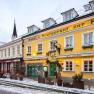 Exterior view of a yellow building with the inscription 'Hotel-Restaurant zur Post' in winter, surrounded by snow and decorated with lights.