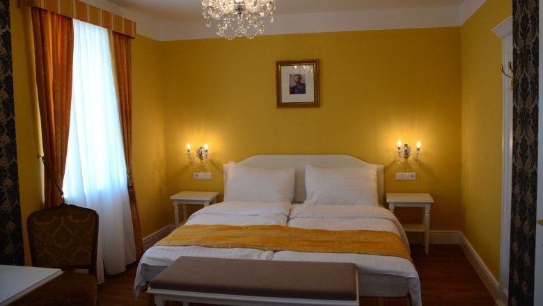 Elegant hotel room with yellow walls, double bed, chandelier and picture on the wall.