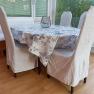 Dining area with table, chairs and bench, tablecloth with floral pattern, window in the background.