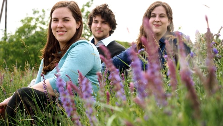 Three young adults sit in a flowering field.
