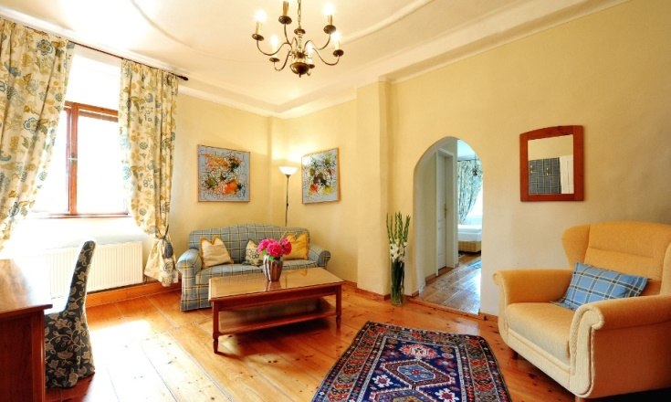 Cozy living room with wooden floor, sofa, armchair, carpet and flowers.