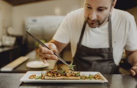 A chef arranges a dish on a plate with a pair of tweezers.