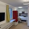 Modern living room with open kitchen, red fridge, yellow curtains and wooden floor.