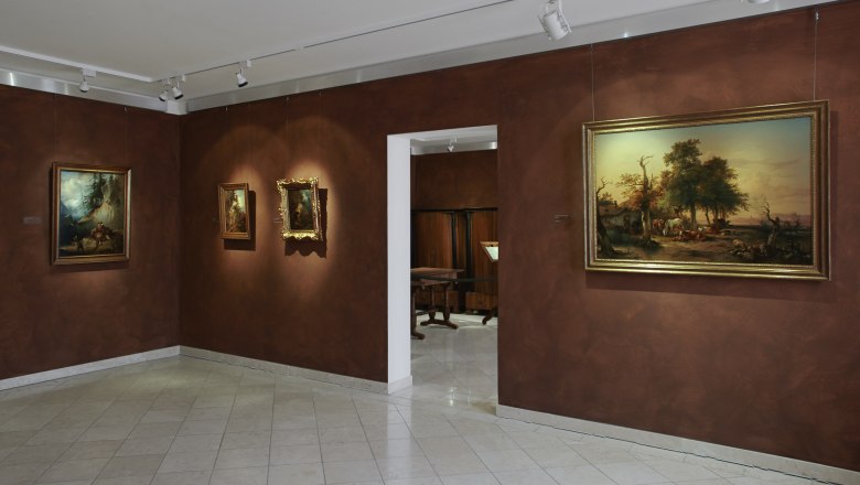 Interior view of a museum with paintings on brown walls.