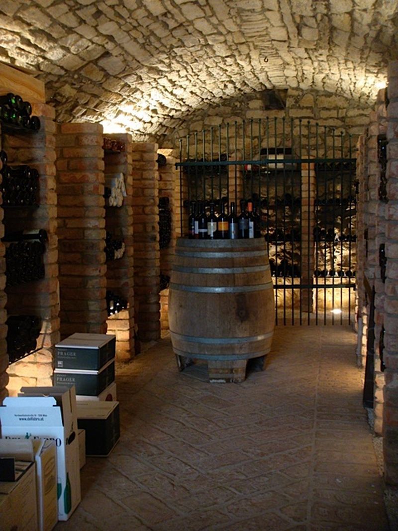 A wine cellar with a vaulted ceiling, wine bottles on shelves and a barrel in the middle.