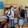 Group of children with suitcases in a dormitory with bunk beds.