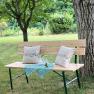 Wooden bench with cushions and tablecloth under a tree in the garden.