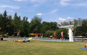 People in the Seebenstein park pool, some on the lawn, others in the pool. A diving tower can be seen.