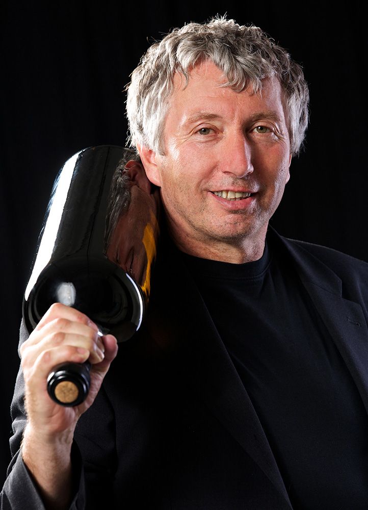Man with gray hair holding a large wine bottle on his shoulder.