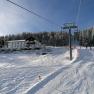 Snow-covered ski slope with ski lift and forest in the background.