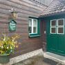 Entrance of a wooden house with green door and window, decorated with an Easter shrub.