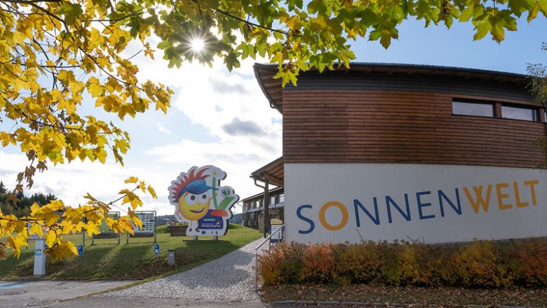 Entrance to SONNENWELT Gro&szlig;sch&ouml;nau with autumnal trees and sunshine.