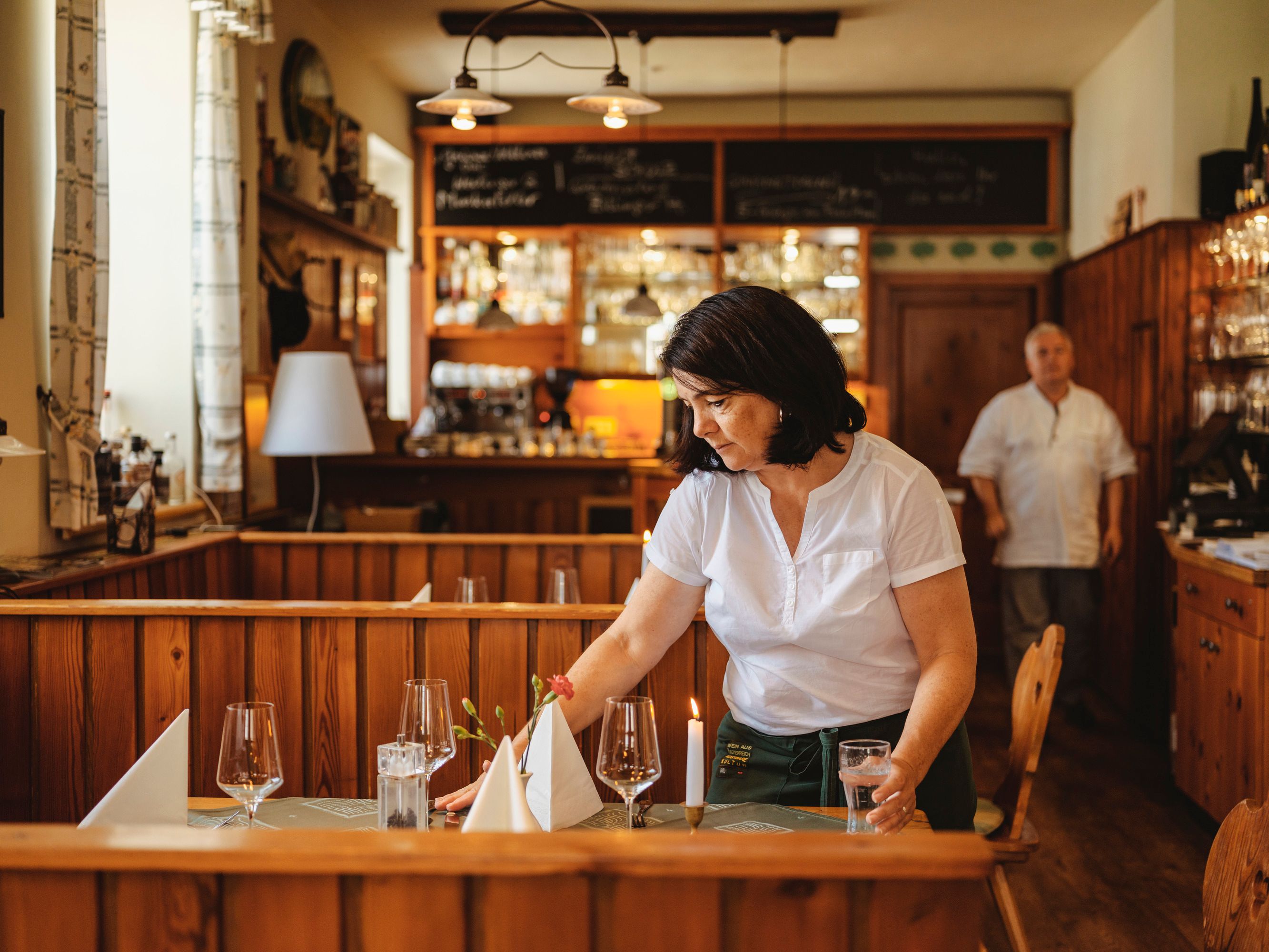 A woman sets a table in a cozy restaurant.