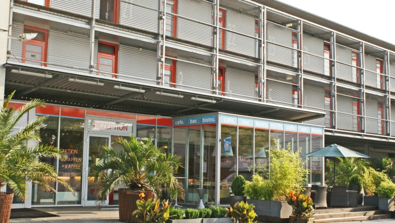 Modern hotel façade with glass front and plants.