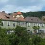 Terraced houses with green facades and red roofs in front of wooded hills.