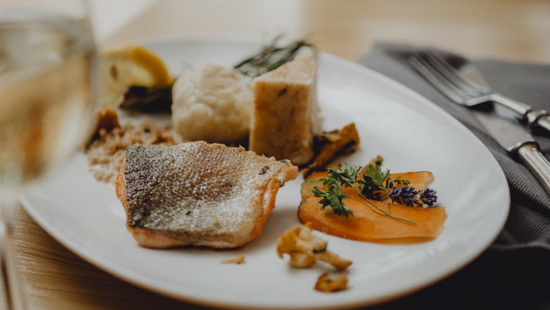 A plate of fried char, porcini mushroom dumplings and vegetables, decorated with herbs.