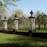 A decorative iron fence with stone pillars and ornate spikes in front of flowering trees in the background.