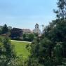 View of a church and a wooden house behind trees and meadows.