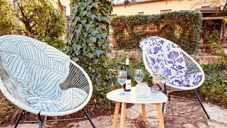 Two chairs with blankets and a table with wine and glasses in a garden.