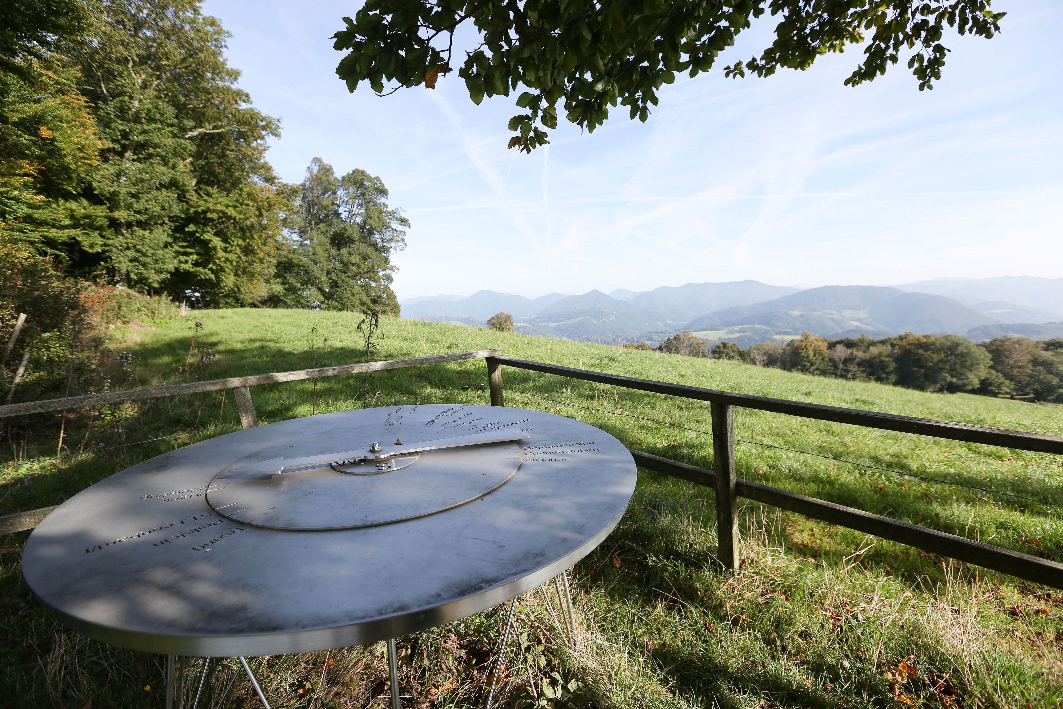 Panoramic view from the Bichlberg with a metal plaque in the foreground and mountains in the background.