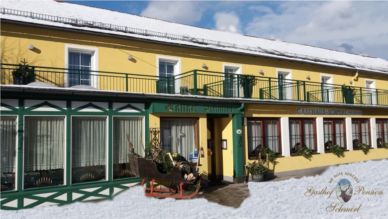 Yellow building with green accents, labeled Gasthof Schmirl, in the snow.