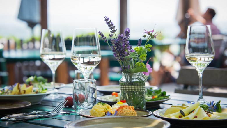 A table set outside with wine glasses, flowers and food.