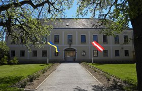 Hochwolkersdorf Castle with two flags, surrounded by trees and lawn.