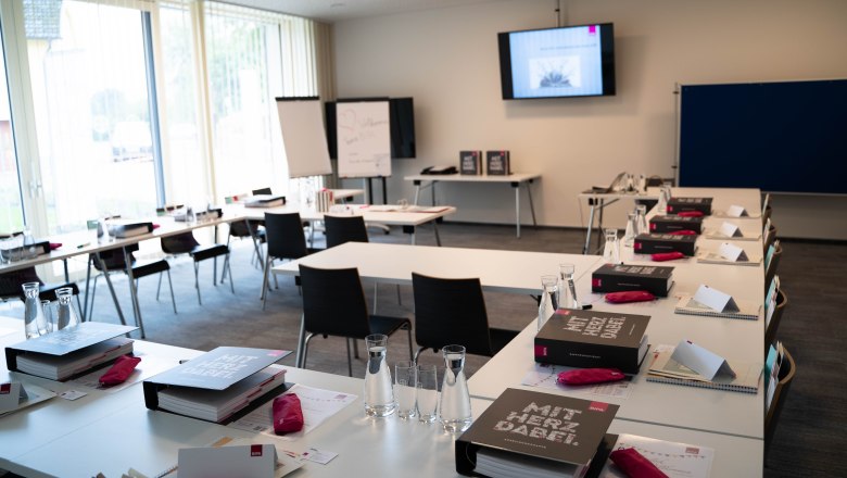 A seminar room with tables, chairs, folders and water bottles, ready for an event.