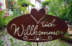 Metal sign with the inscription 'Welcome' in a garden.