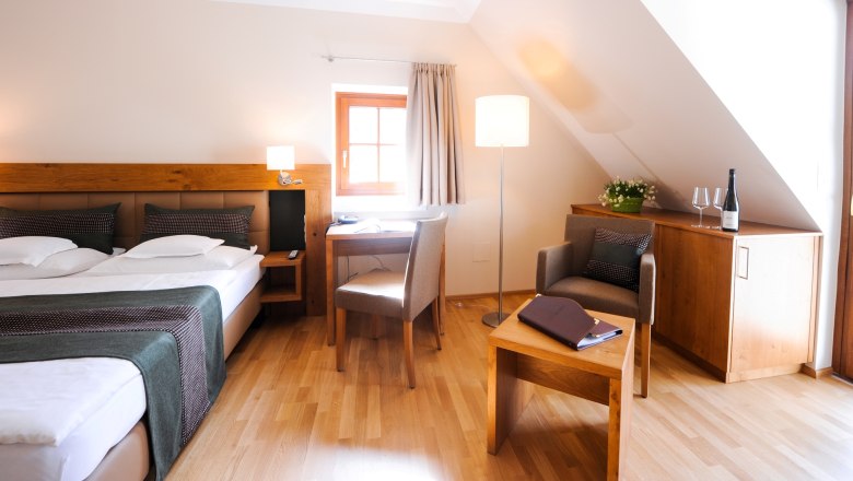 Cozy hotel room with double bed, desk, armchair and bottle of wine on a cupboard.