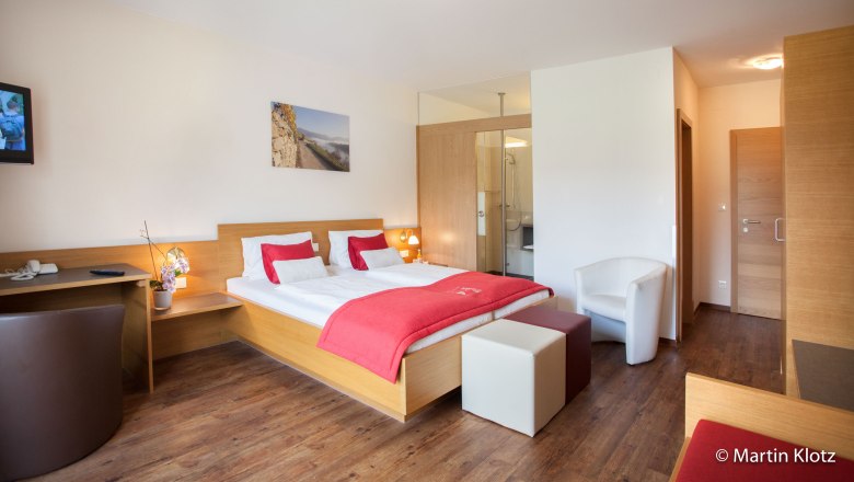 Modern hotel room with double bed, red accents, desk and TV.
