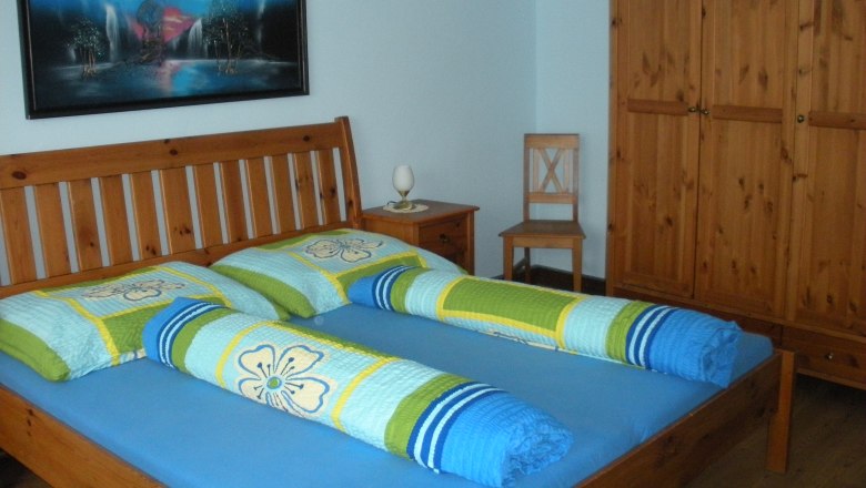 A guest room with a wooden bed, colorful comforters, a wardrobe and a picture on the wall.