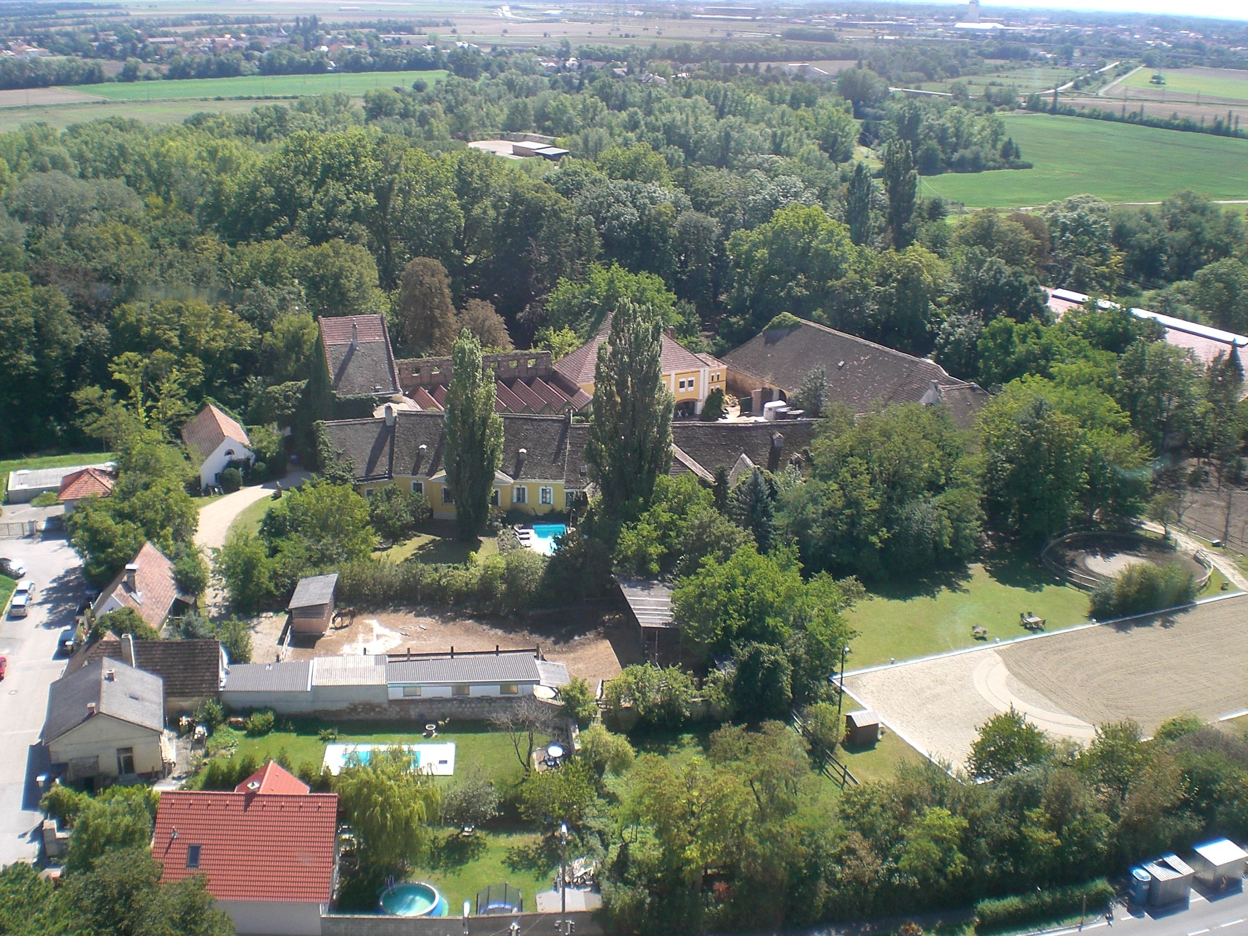 Aerial view of a riding stable with buildings, trees and riding arena.