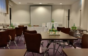 Seminar room with tables, chairs and drinks, projection screen in the background.