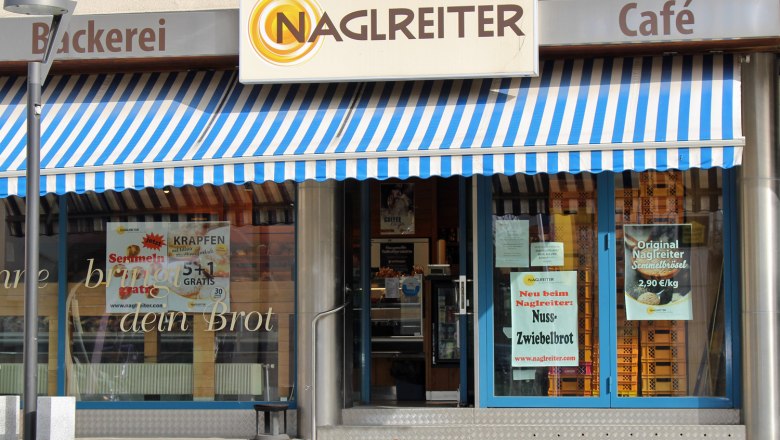 Entrance of a bakery with blue and white striped awning and signs for special offers.
