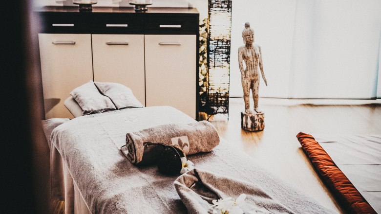 A spa room with massage table, towels, Buddha statue and candles.