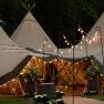 An illuminated teepee tent for an event, surrounded by plants and fairy lights.