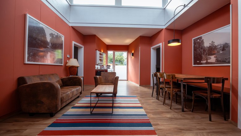 Interior view of a living room with red walls, leather sofa, wooden table and colorful carpet.
