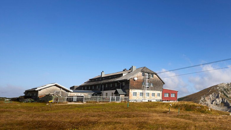 Panoramic view of a mountain hut with surrounding peaks under a blue sky.