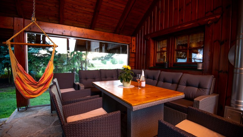 Covered terrace with wooden table, rattan furniture and hanging chair.