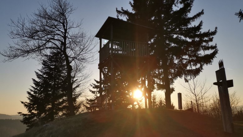 Sunset behind a lookout tower and trees.