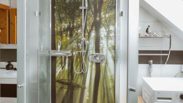 Shower area with forest picture on the back wall, washing machine next to it.