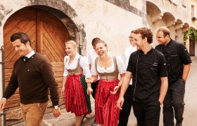 Group of people in traditional clothing and cooking uniforms in front of an old building.