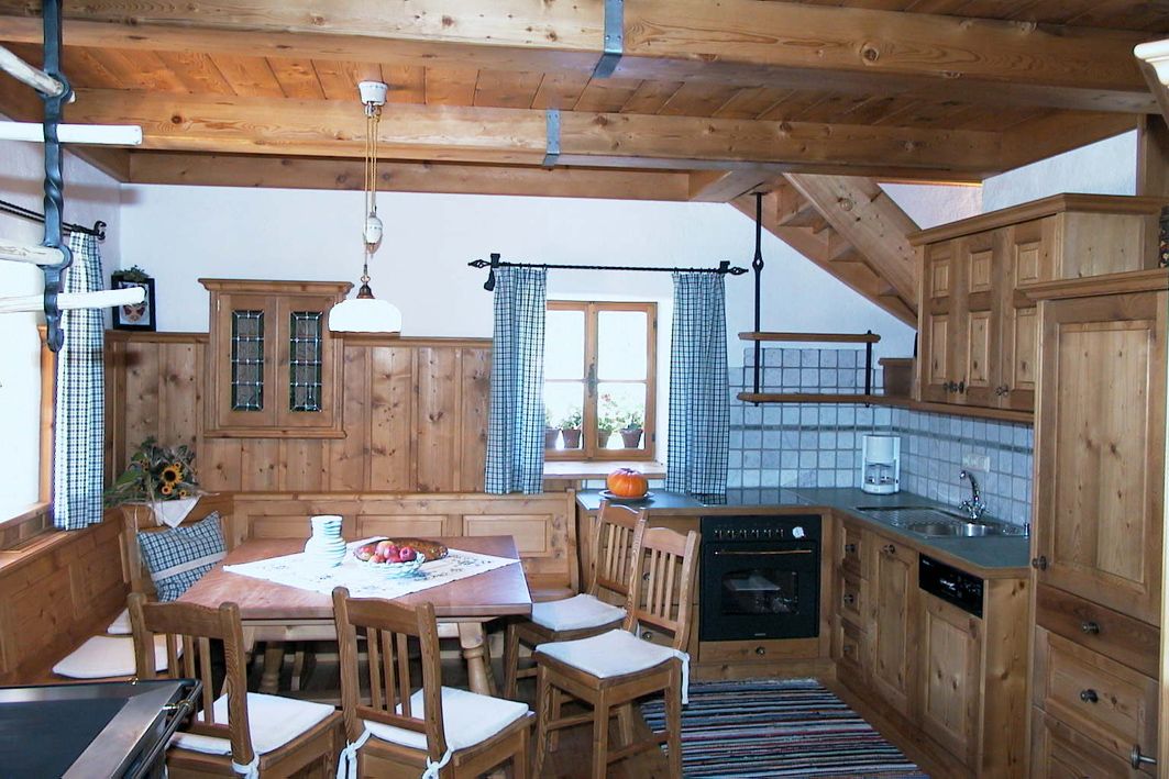 Rustic kitchen with wooden furniture, dining table and chairs, stove, sink and window with checkered curtains.