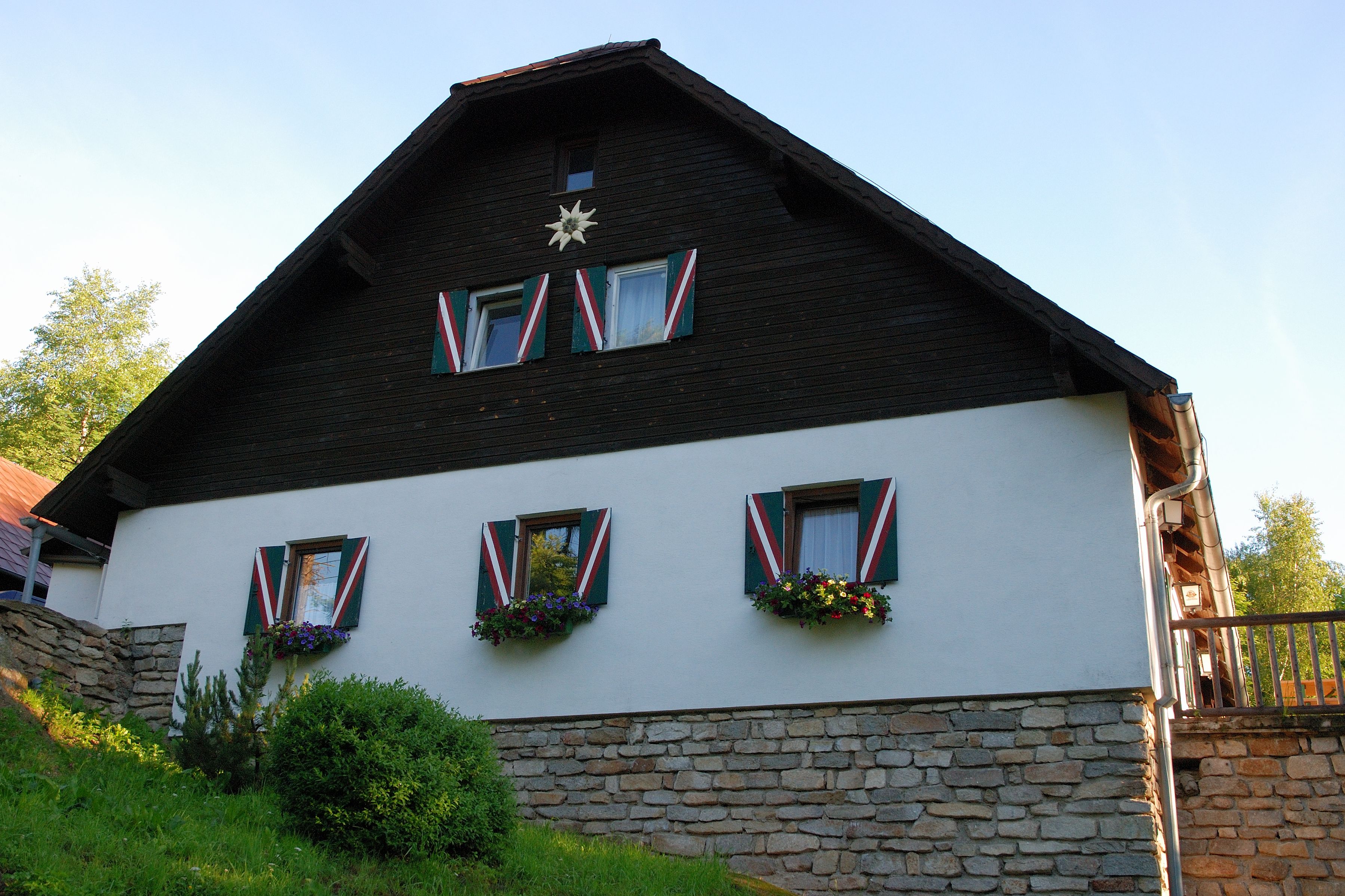 A traditional house with wooden cladding and colorful shutters, surrounded by green vegetation.