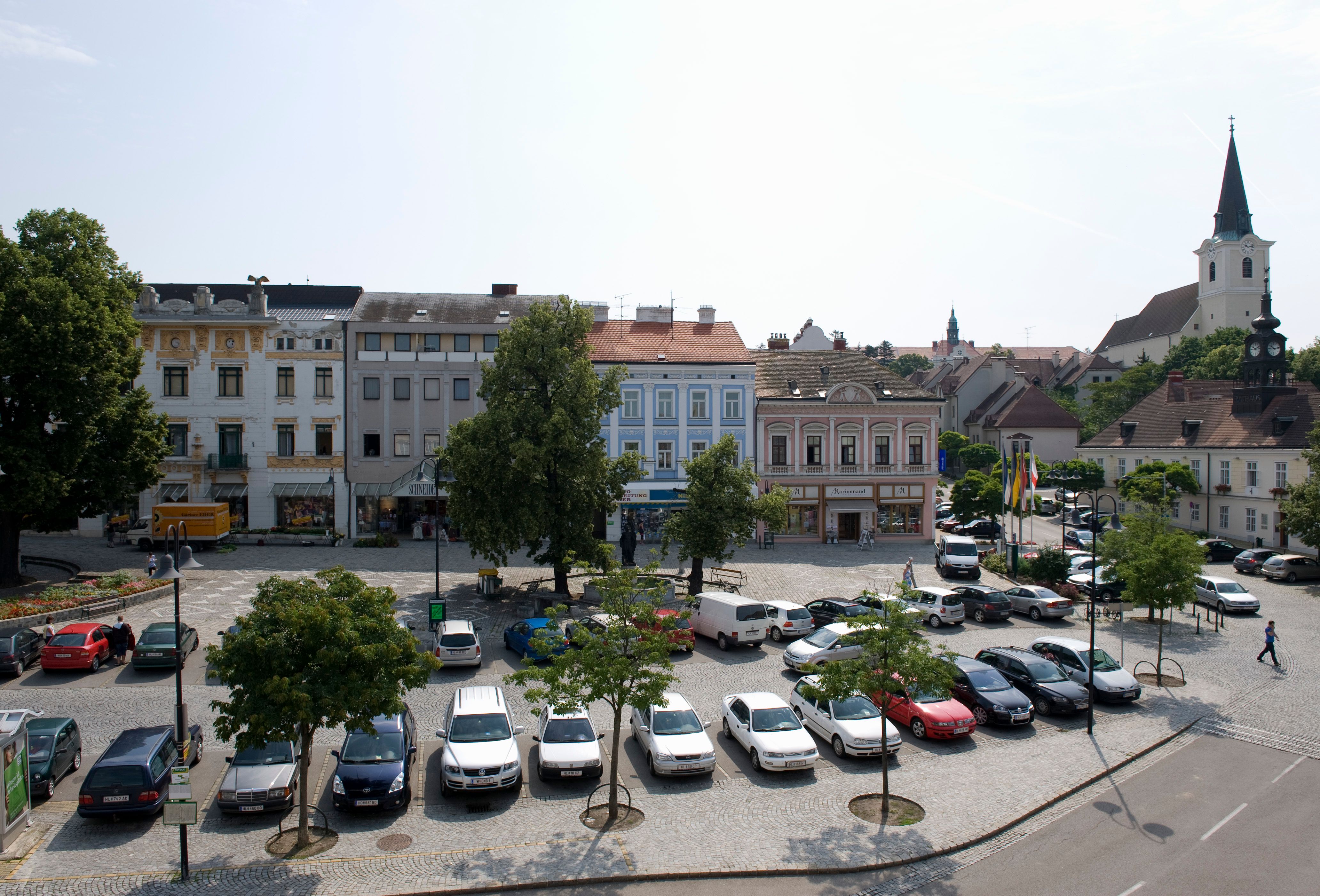 Town square in Hollabrunn with parked cars, historic buildings and a church in the background.