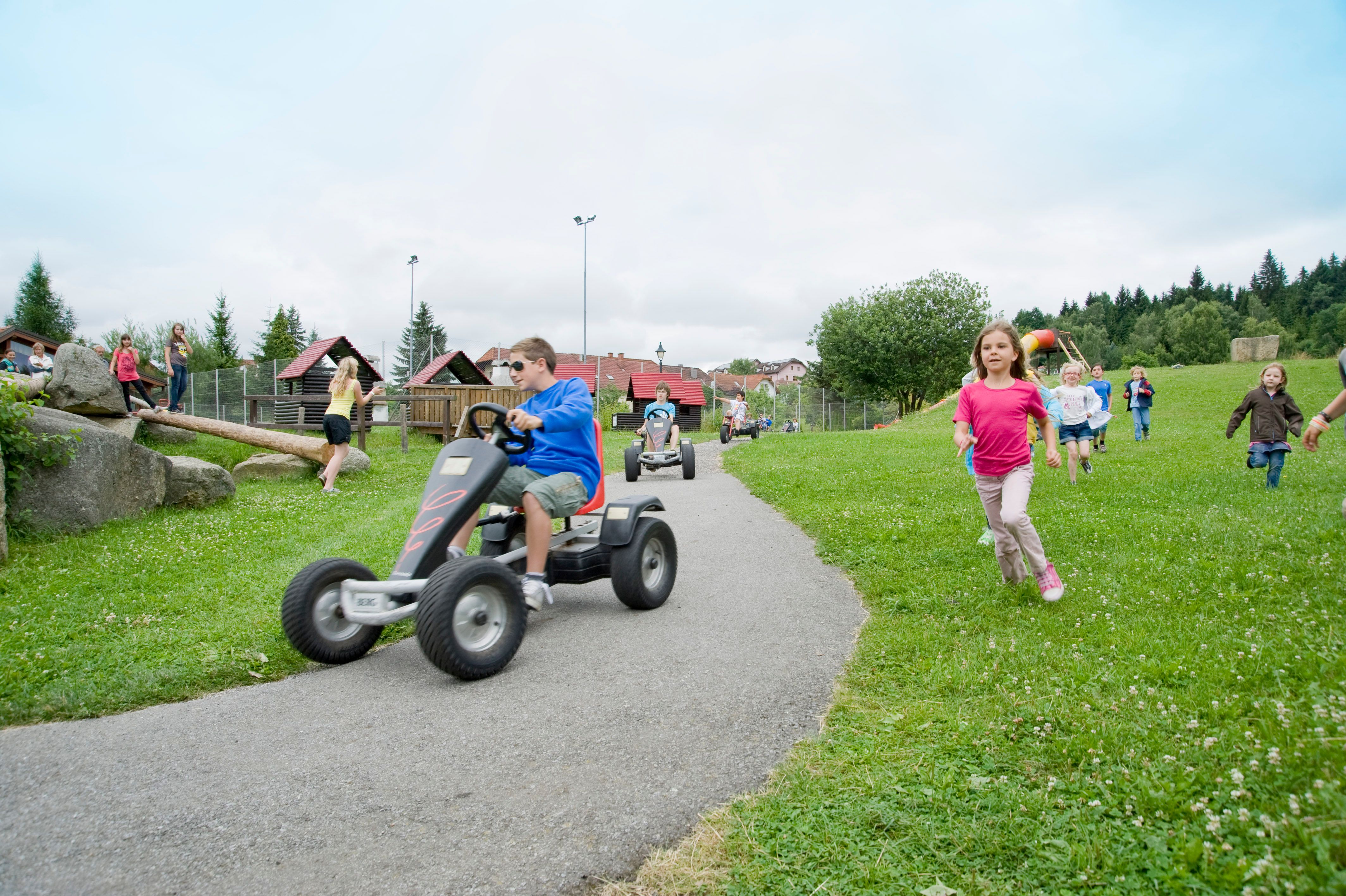 Children play on an adventure playground with Kettcars and run across a meadow.
